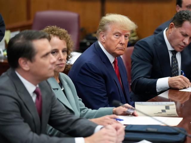 Former President Donald Trump sits at the defense table with his defense team in a courtroom.