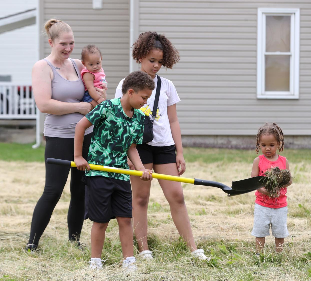 Braxton Robert, 8, turns over a shovel full of dirt as his family members, from left, mother Sara Kurzinky, holding sister Halo Cooper, 10 months; Bri'Elle Robert, 10; and brother Kendrixx Cooper, 3, look on Monday, June 17, 2024, during a groundbreaking ceremony at the site of their new home at Green Avenue and Noble Street in Alliance.