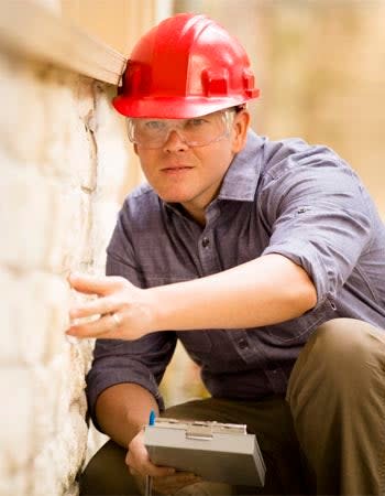 A person in a red hard hat examines a brick wall.