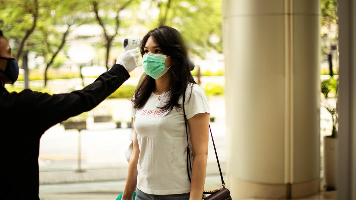 security guard measuring temperature of young woman  with infrared thermometer before entering a office, in Jakarta.