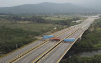 This image taken from video, shows a fuel tanker, cargo trailers and makeshift fencing, blocking the Tienditas International Bridge in an attempt to stop humanitarian aid entering from Colombia, as seen from the outskirts of Cucuta, on Colombia's border with Venezuela, Wednesday, Feb. 6, 2019. Immigration authorities say the Venezuelan National Guard built the roadblock a day earlier. (AP Photo)
