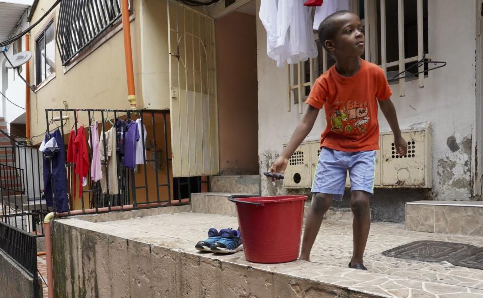 A boy with a red bucket in front of a house.