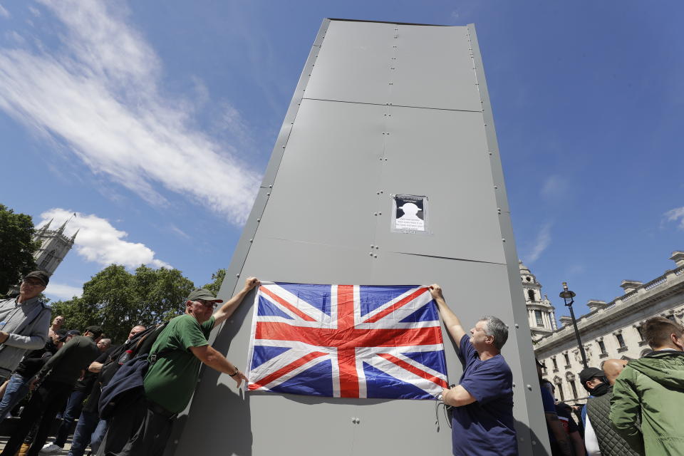 Members of far-right Football Lads Alliance hold a British flag in front of a protective covering surrounding the statue of former British Prime Minister Sir Winston Churchill in Parliament Square, central London, Saturday, June 13, 2020. British police have imposed strict restrictions on groups planning to protest in London Saturday in a bid to avoid violent clashes between protesters from the Black Lives Matter movement, as well as far-right groups.(AP Photo/Kirsty Wigglesworth)