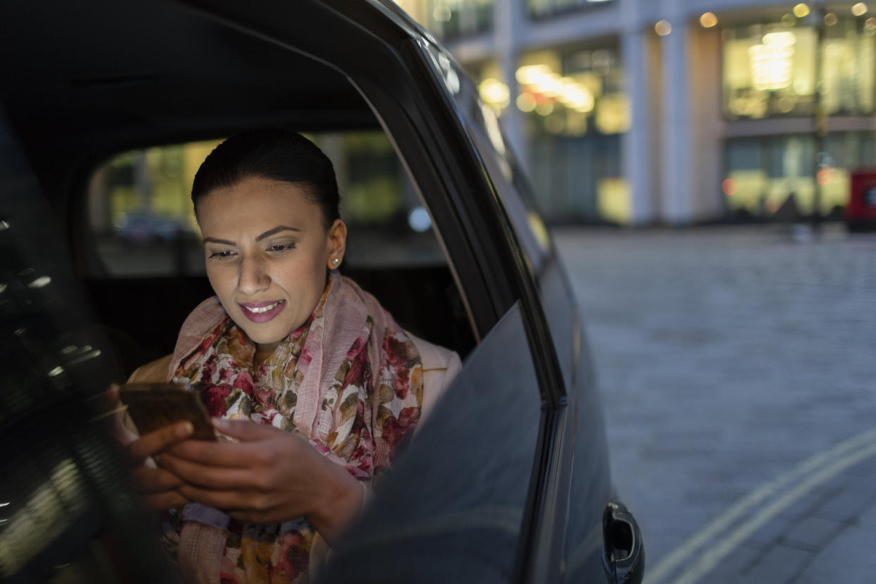 Businesswoman using smart phone in crowdsourced taxi at night