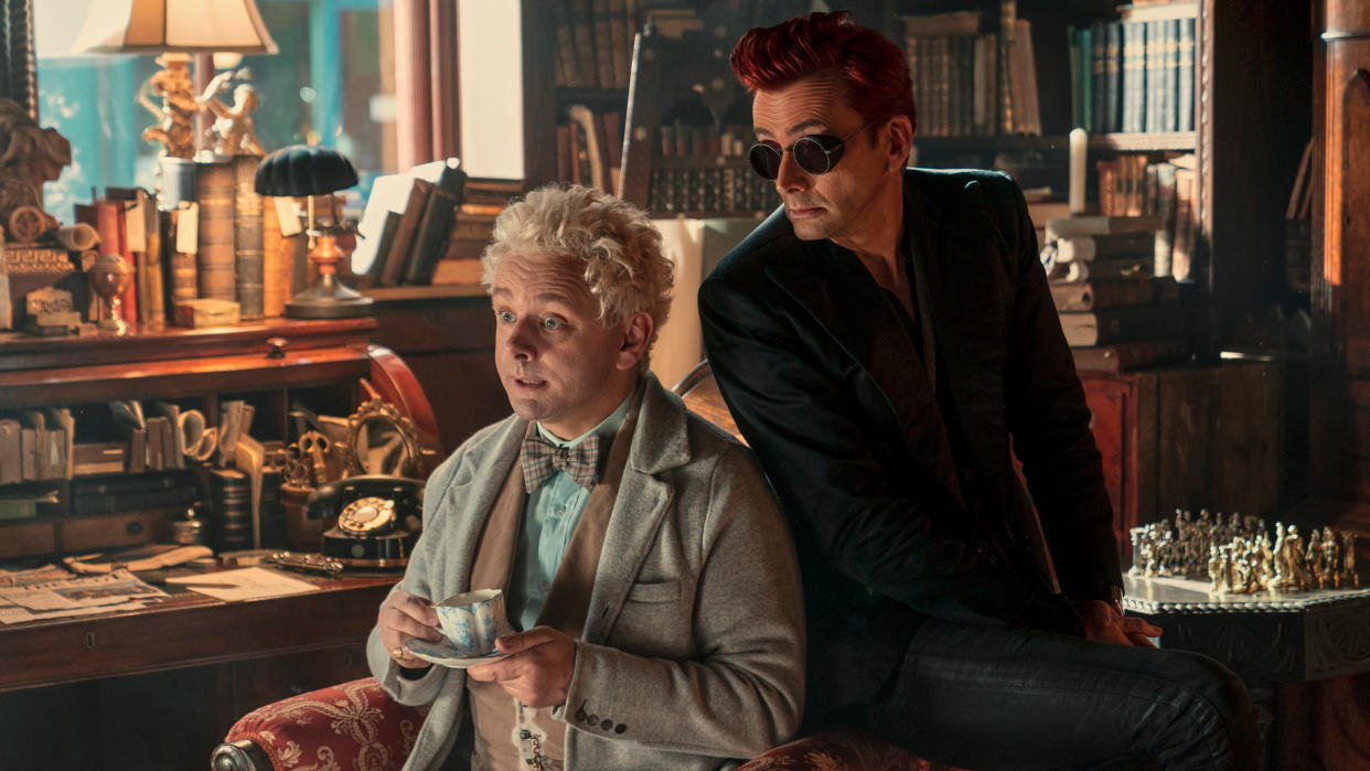  Aziraphale sits with a cup of tea and Crowley perches on the arm of the chair in Good Omens season 2 episode 3. 