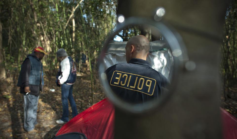 In this Friday, Dec. 13, 2013 photo, Savannah's Homeless Liaison Officer Tom Gentner's is reflected in the shaving mirror of a homeless man at Camp 7 in Savannah, Ga. Residents call the area the "Bamboo Forest" because of the acres of the dense plants which conceal their community of fenced off encampments. (AP Photo/Stephen B. Morton)