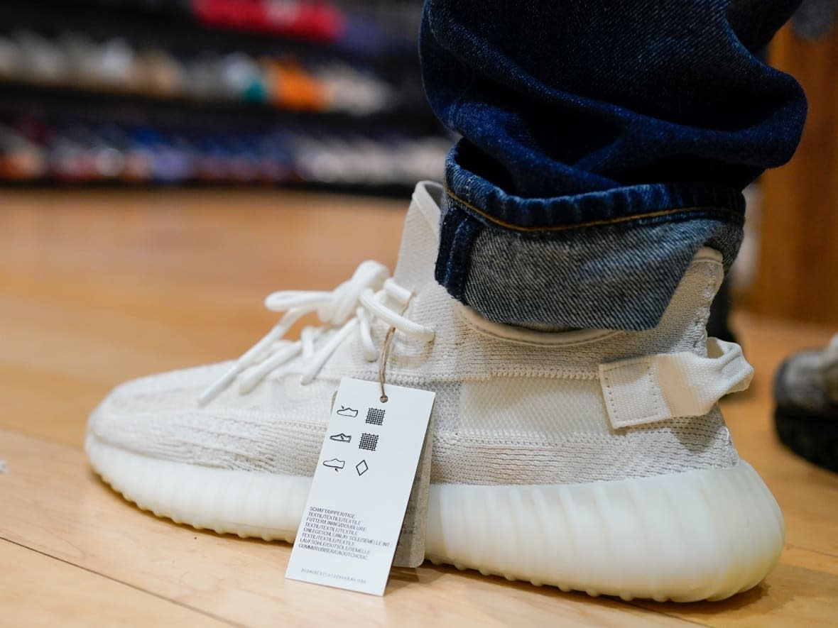 A customer tries on Yeezy shoes, made by Adidas in partnership with Kanye West, at a sneaker resale store in Paramus, N.J., on Tuesday. That same day, Adidas ended its partnership with the rapper over antisemitic remarks he made. Now the controversy has some sneakerheads contemplating parting with their collectible kicks.  (Seth Wenig/The Associated Press - image credit)
