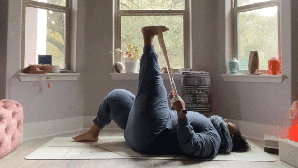 Woman lying on her back in her bedroom stretching her hamstrings