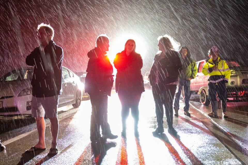 People stand on a road with stopped cars at night.