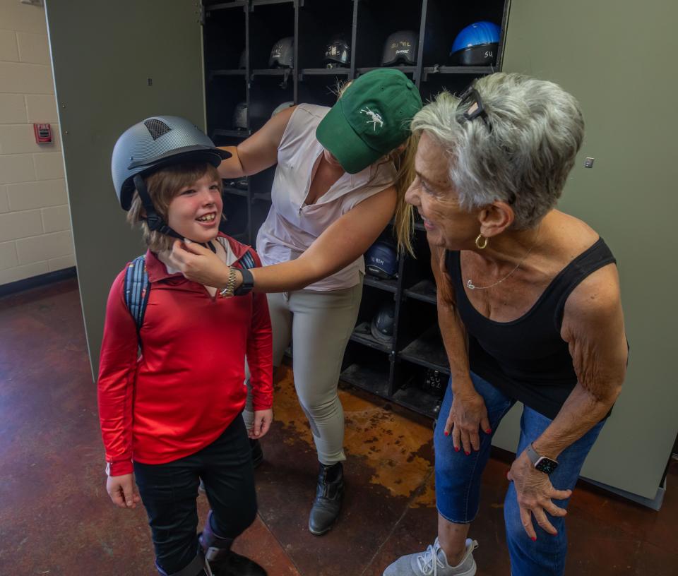 Instructor Lindsey Landrum helps Ephraim Lober get ready for horse therapy at Saddle Up! in Franklin. At right is volunteer Fern Aron.