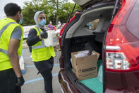 In this Thursday, May 28, 2020, photo, a volunteer places groceries in the trunk of a car during a food distribution drive sponsored by Island Harvest Food Bank in Valley Stream, N.Y. (AP Photo/Mary Altaffer)