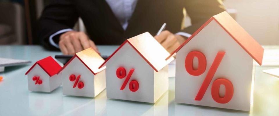 Close-up Of A House Models With Percentage Symbol In Front Of Businessperson Working In Office