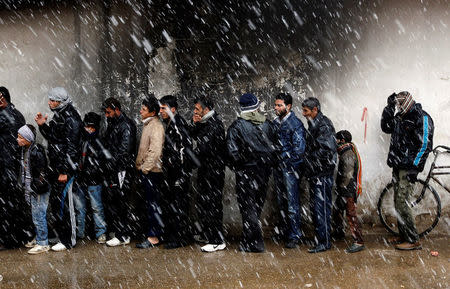 FILE PHOTO: Men wait to buy bread in front of a bakery shop during winter in Al Qusayr, a city in western Syria about 4.8km (3 miles) southwest of Homs, March 1, 2012. REUTERS/Goran Tomasevic/File Photo