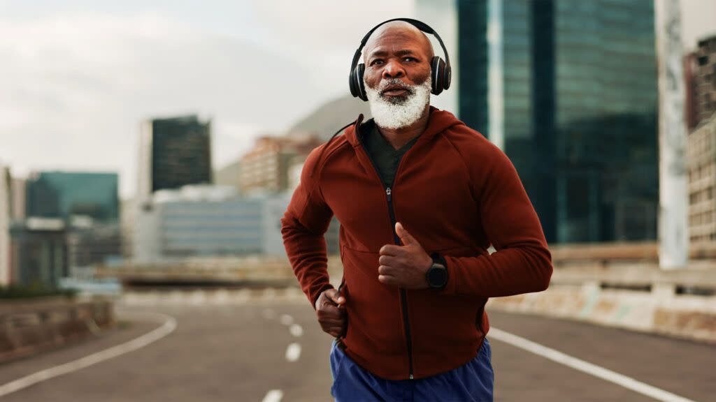 An older man wearing headphones jogs on a track