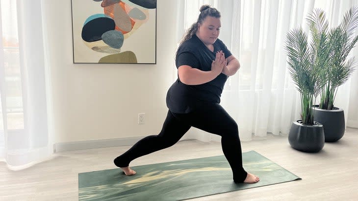 A woman on a yoga mat practicing a body positive yoga pose by twisting while standing upright rather than bent over the thigh.