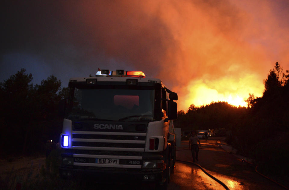 A fire fighter approaches a fire engine along a mountain road as the front of a huge wildfire in the foothills of the Pentadaktylos mountain range is seen in the distance in the breakaway north of ethnically divided Cyprus on Thursday, June 23, 2022.Israel on Thursday dispatched two water-dropping aircraft to help in fighting the wildfire that has scorched at least 10,000 acres (4,000 hectares) of forest.(AP Photo/Nedim Enginsoy)