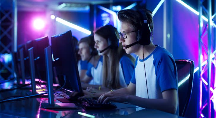 A row of people wearing matching outfits and headsets play a video game together in a room with blue lighting.