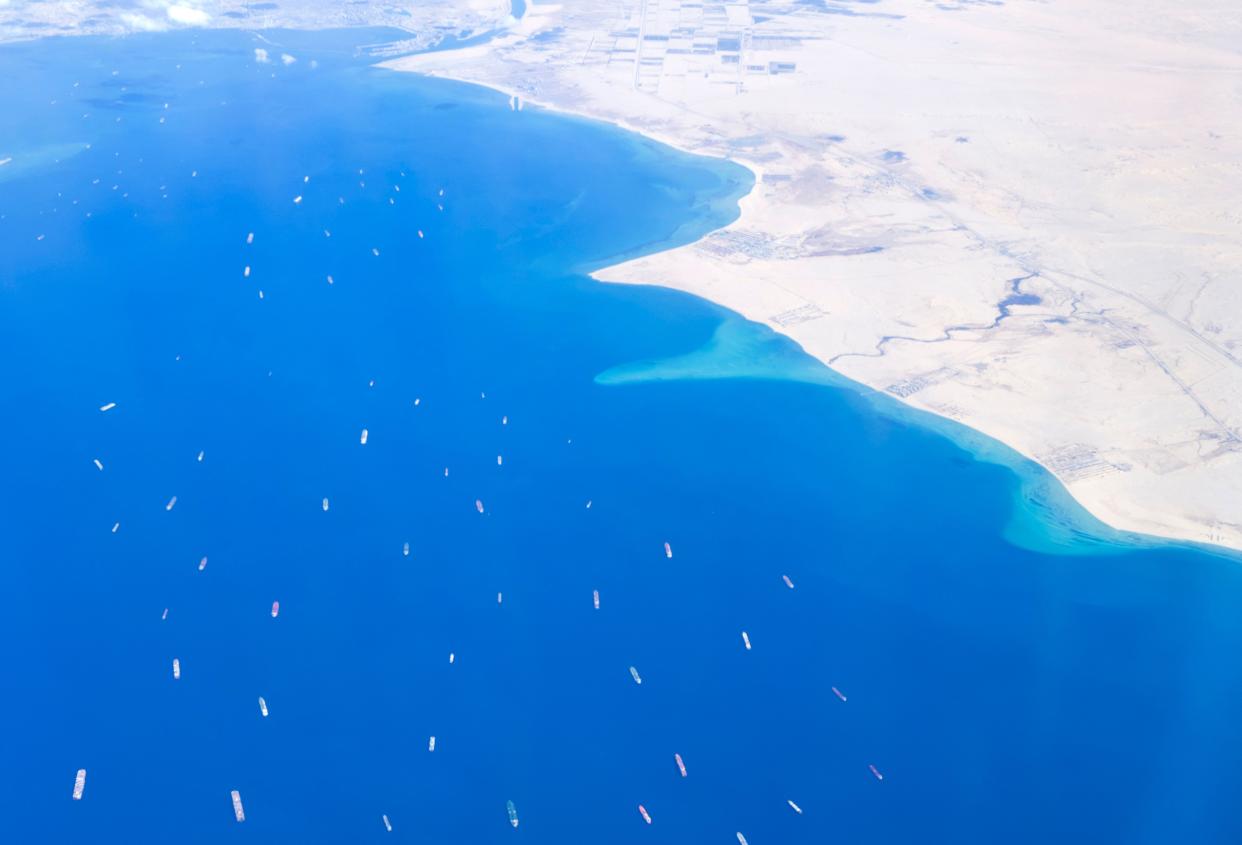 An aerial view taken on March 27, 2021, from the porthole of a commercial plane shows stranded ships waiting in a queue in the Gulf of Suez to cross the Suez Canal at its southern entrance near the Red Sea port city of Suez, as the waterway remains blocked by the Panama-flagged container ship "MV Ever Given," which has remained wedged sideways about six kilometers north of the canal's entrance, impeding all flowing traffic since March 23.