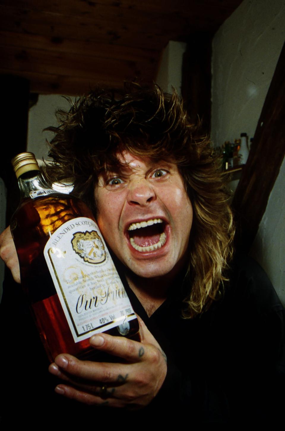 Ozzy Osbourne holding a large bottle of whisky at his home, May 1989. (Photo by People/Mirrorpix/Getty Images)