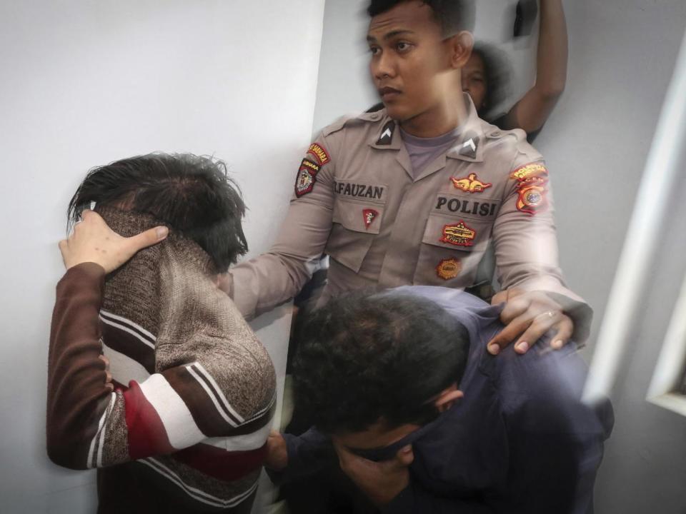A police officer escorts two men accused of having gay sex into a holding cell prior to their trial at sharia court in Banda Aceh (AP)