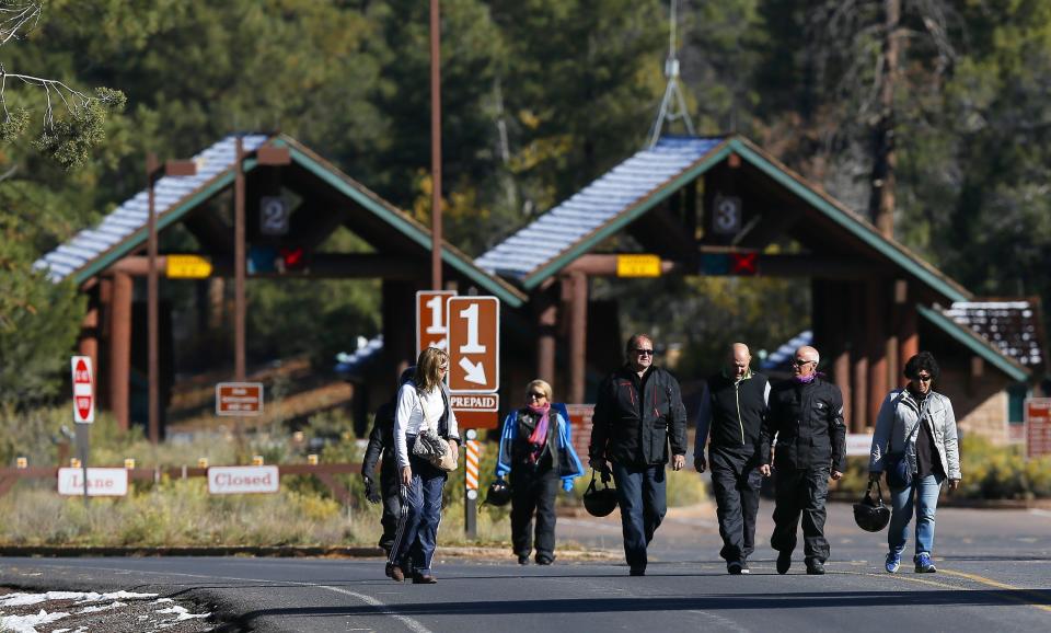 FILE - A group of motorcyclists from France walk back out from the main entrance to Grand Canyon National Park after they learned they were not allowed to enter the park as it remains closed due to the government shutdown, in October 2013. Arizona's Grand Canyon National Park and all five national parks in Utah will remain open if the U.S. government shuts down, Sunday, Oct. 1, 2023. Arizona Gov. Katie Hobbs and Utah Gov. Spencer Cox say that the parks are important destinations and local communities depend on dollars from visitors.(AP Photo/Ross D. Franklin, File)