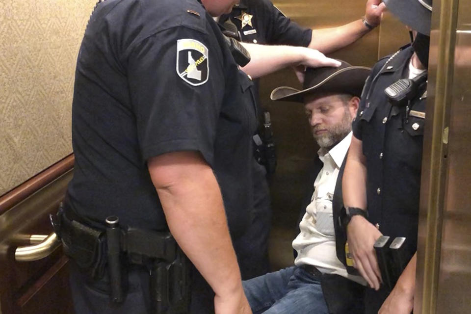 This image taken from video shows anti-government activist Ammon Bundy, rear, being wheeled into an elevator in a chair following his arrest at the Idaho Statehouse in Boise, Idaho, Tuesday, Aug. 25, 2020. Authorities arrested Bundy after he refused to leave a meeting room where a few hours earlier angry protesters forced out lawmakers. (AP Photo/Keith Ridler)