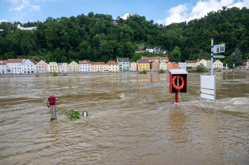 A fire hydrant and a lifebuoy holder stick out of the water of a flooded street in the city on the three rivers.  After heavy rainfall, many places in Bavaria remain flooded.  Peter Kneffel/dpa