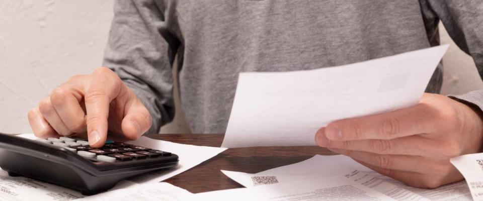 Man hands, a finger on button of calculator with financial documents in a hand and others on the table