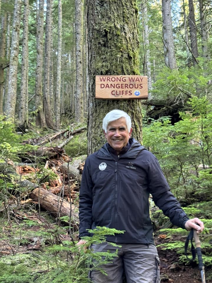 North Shore Rescue's Wally Kerchum poses in front of sign erected to warn people away from a non-existent trail that appeared on Google Maps.