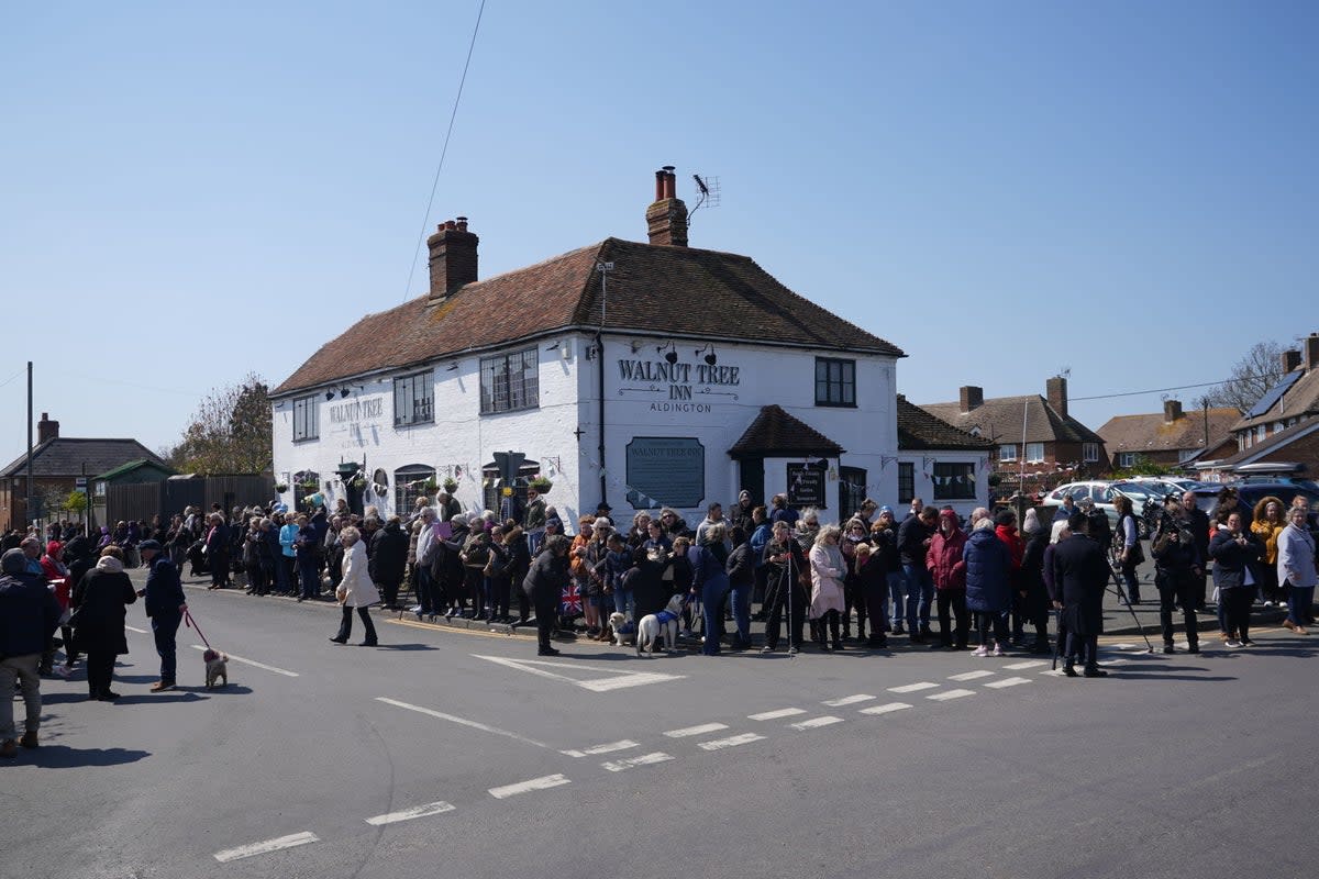 Mourners gather outside the Walnut Tree Pub in Aldington (PA)