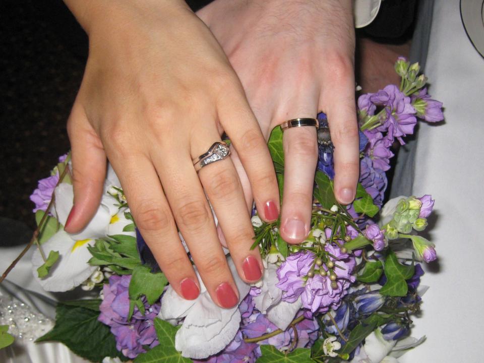 Stacy Brooks hand over a bouquet of flowers with her wedding ring, and her husband's hand with his wedding ring.