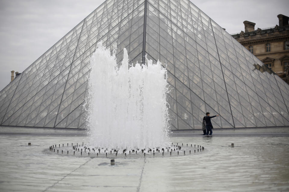 Tourists walk at the bottom of the pyramide of the Louvre museum, in Paris, Friday, May 17, 2019. Paris' Louvre museum is paying tribute to the architect of its giant glass pyramid, I.M. Pei, who has died at age 102. (AP Photo/Thibault Camus)