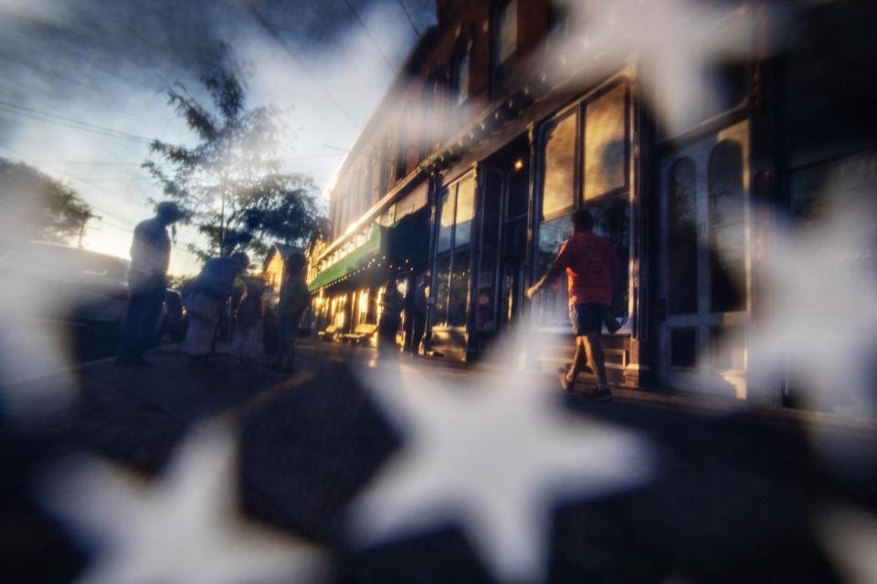 The sun sets on Main Street, as seen through a U.S. flag, Saturday, Aug. 31, 2019, in Trumansburg, N.Y., where earlier in the day a memorial procession passed through for Sgt. James Johnston, who was killed in Afghanistan in June. Two months after his death, his adopted hometown had come together over a holiday weekend to pay tribute, and to say goodbye. (AP Photo/David Goldman)