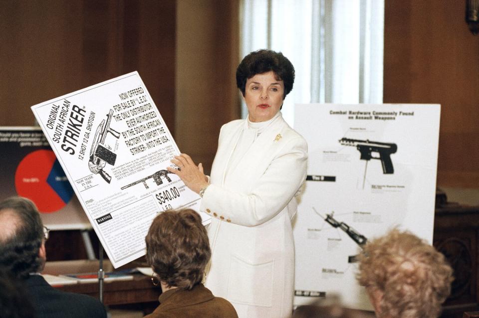 A woman dressed in white holds up an advertisement for a shotgun at a news conference