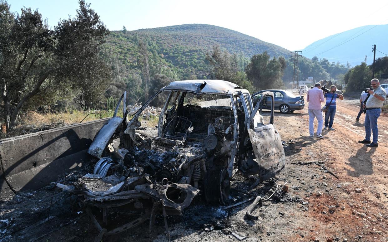 A burnt out car sits at the edge of a road