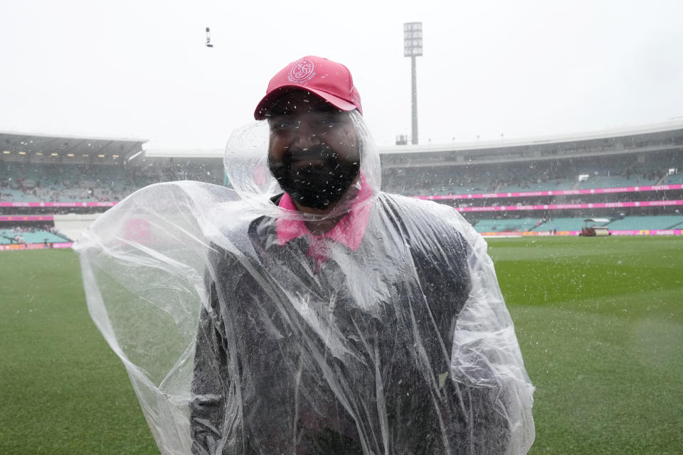 A security guard stands on the boundary of the field as rain falls during the third day of the cricket test match between Australia and South Africa at the Sydney Cricket Ground in Sydney, Friday, Jan. 6, 2023. (AP Photo/Rick Rycroft)