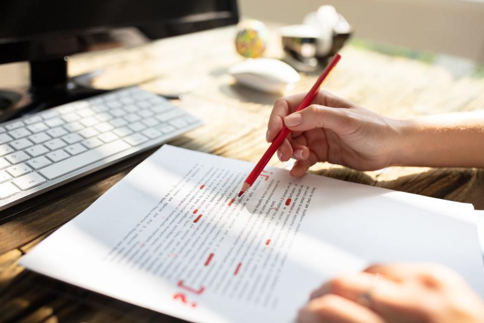 A person marking errors on a printed document with a red pen.