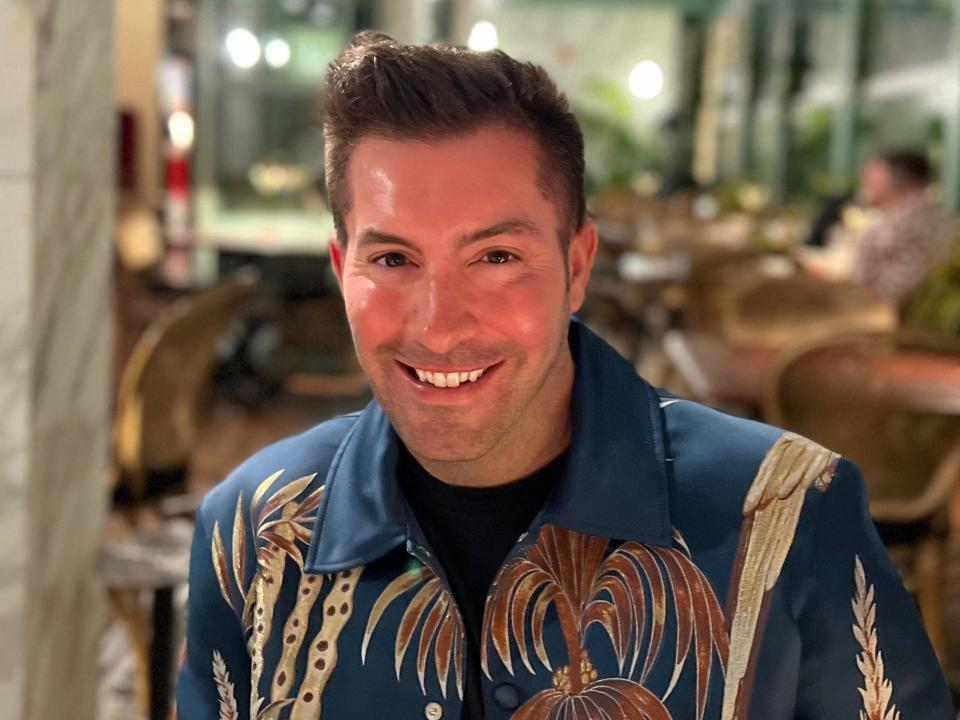 A man with a designer jacket posing for the camera in a restaurant.