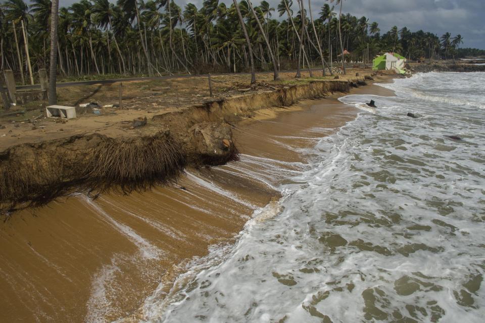 Waves lap against an eroded shoreline with Ranjith Sunimal Fernando's family home visible in the distance in Iranawila, Sri Lanka, Monday, June 19, 2023. Much like the hundreds of other fishing hamlets that dot the coastline, the village of Iranawila suffers from coastal erosion. (AP Photo/Eranga Jayawardena)