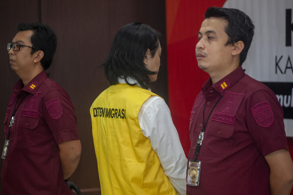 Indonesian Immigration officers flank Yusuke Yamazaki, center, a Japanese fugitive who is wanted for fraud in his home country, as he is presented during a press conference prior to his deportation in Batam, Indonesia, Tuesday, March 12, 2024. (AP Photo/Andaru Kz)