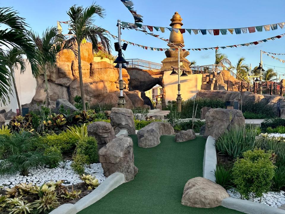 mini golf area with green turf. surrounded by rocks and palm trees