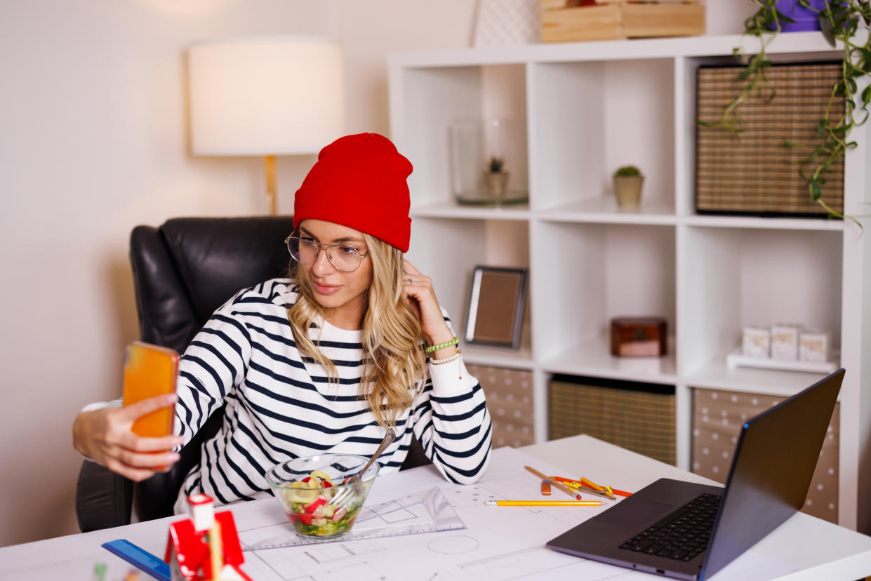 Young female interior designer eating salad and using her phone for two-factor authentication. 