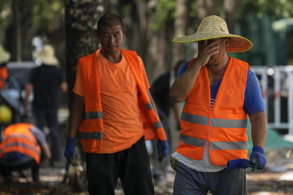 A worker wipes his sweat as he and his co-workers place tiles on a pavement on a sweltering day in Beijing, Monday, July 10, 2023. Rescuers were looking Monday for several people missing in a landslide triggered by torrential rains while employers across much of China were ordered to limit outdoor work due to scorching temperatures as the country struggled with heat, flooding and drought. (AP Photo/Andy Wong)