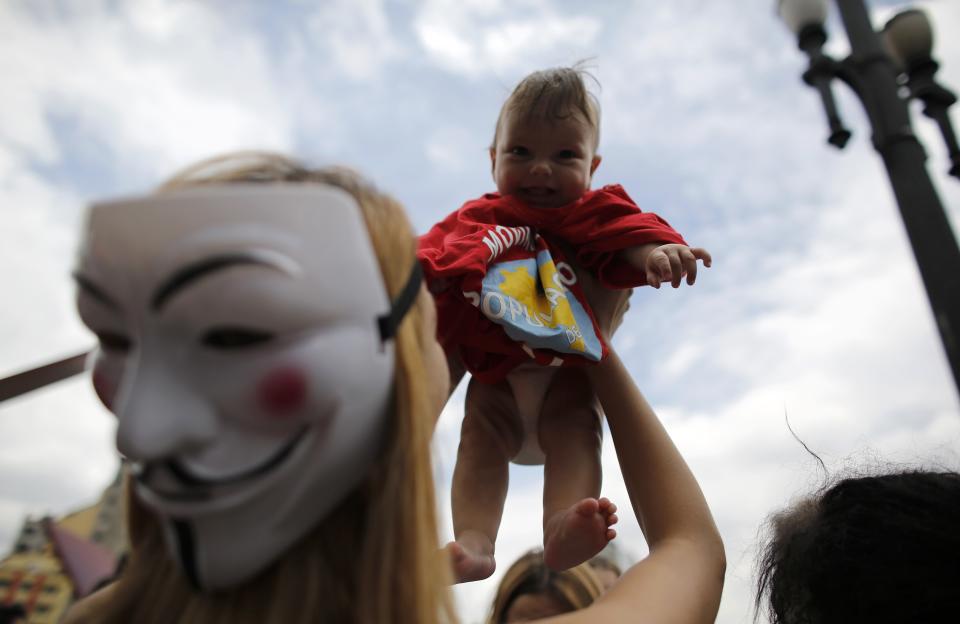 Woman, wearing a Guy Fawkes mask, holds up a homeless child during a Christmas street celebration in downtown Sao Paulo