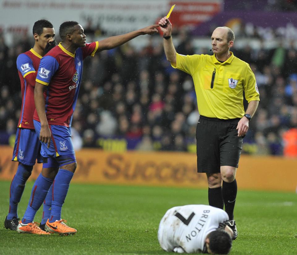 Referee Mike Dean, right, shows a yellow card to Crystal Palace's Mile Jedinak, not pictured, during the English Premier League soccer match between Swansea City and Crystal Palace at the Liberty Stadium, Swansea, Wales, Sunday, March 2, 2014. (AP Photo/PA) UNITED KINGDOM OUT - NO SALES - NO ARCHIVES