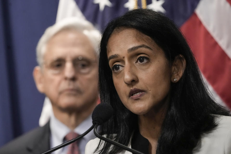 Merrick Garland stands just behind Vanita Gupta as she speaks into a microphone.