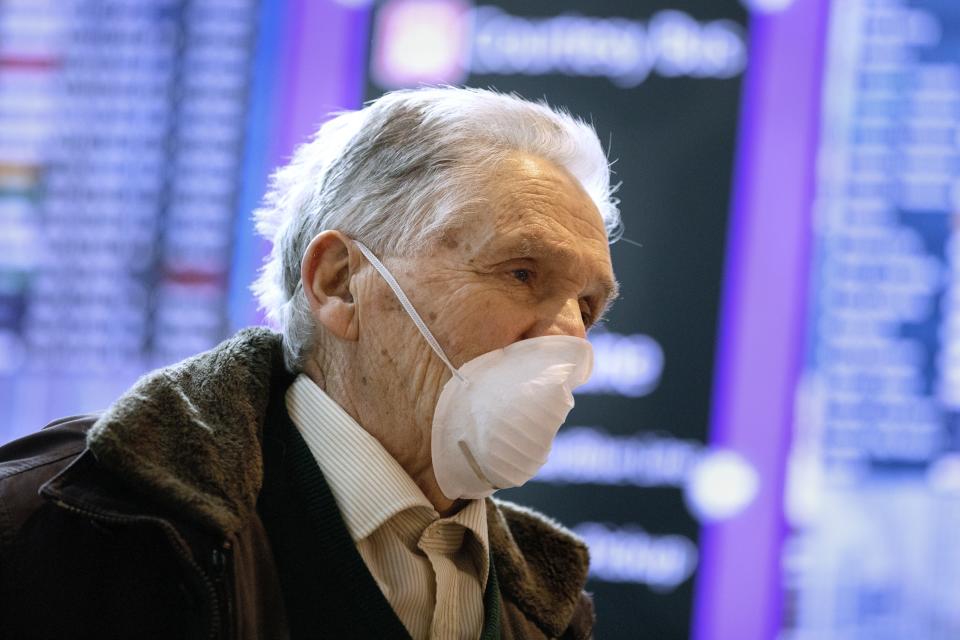 A passenger who arrived on a flight from Germany stands in front of a flight information board at Logan International Airport in Boston, Friday, March, 13, 2020. Beginning at midnight Friday most Europeans will be banned from entering the United States for 30 days to try to slow down the spread of the coronavirus. Americans returning from Europe will be subject to enhanced health screening. For most people, the new coronavirus causes only mild or moderate symptoms, such as fever and cough. For some, especially older adults and people with existing health problems, it can cause more severe illness, including pneumonia. The vast majority of people recover from the new virus. (AP Photo/Michael Dwyer)