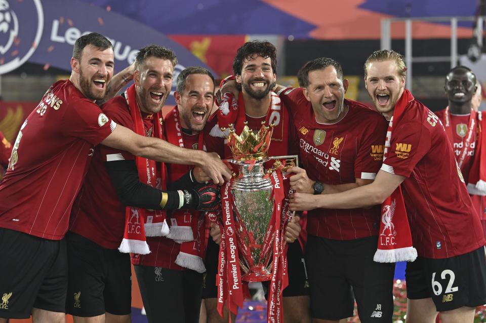 Alisson, center, holds the Premier League trophy surrounds by smiling Liverpool teammates and staff.