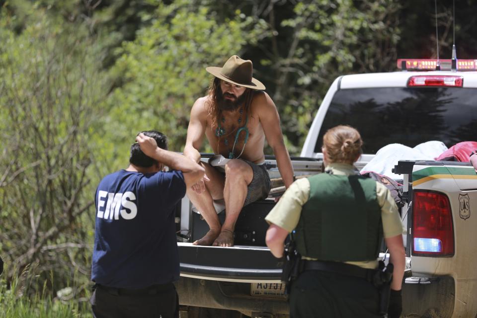 Physician John Hartberg, left, speaks to county and federal officials about an elderly patient being rushed out of a remote encampment on Friday, July 2, 2021, in the Carson National Forest, outside of Taos, N.M.. Hartberg, from New Orleans, was attending the annual Rainbow Gathering where the man fell ill. The condition of the man was not immediately known. (AP Photo/Cedar Attanasio)