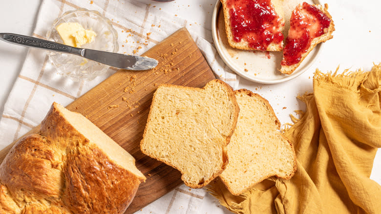 Brioche bread sliced with a side of butter and knife and one slice with jam on top